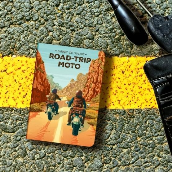 Carnet de voyage « Road-Trip Moto » posé sur une route avec marquage jaune.