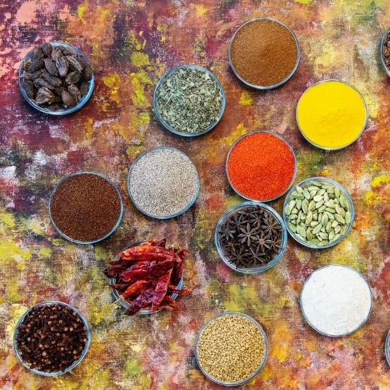 Diverses épices colorées présentées dans des petits bols sur un fond artistique.