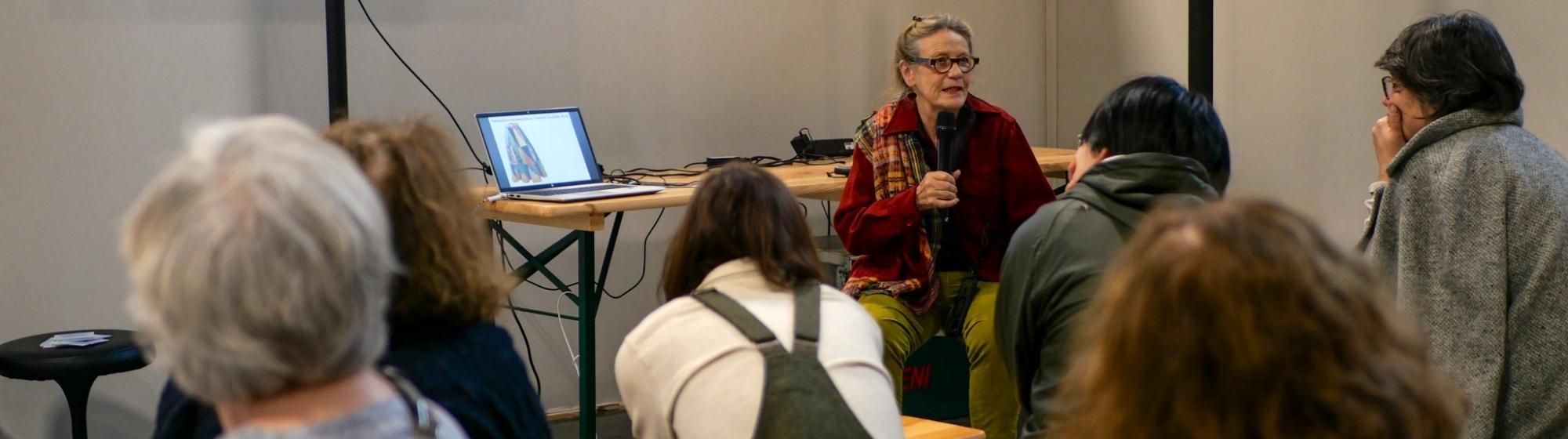 Conférencière animant un atelier sur le patchwork devant un public, avec un écran projetant une œuvre de patchwork.