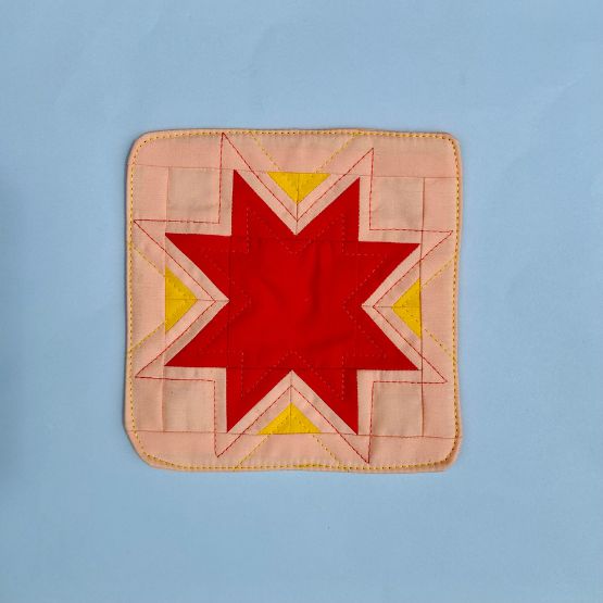 Carré de patchwork avec étoile rouge et jaune sur fond rose.