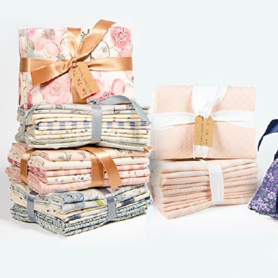 Piles de tissus pliés aux motifs variés, attachés avec des rubans et étiquettes kraft.