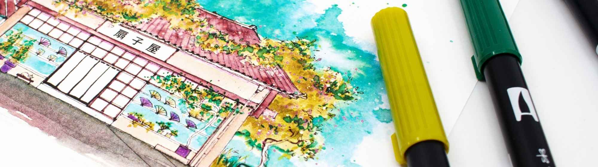 Gros plan d’une aquarelle japonaise colorée représentant une maison traditionnelle, entourée de marqueurs de couleur.
