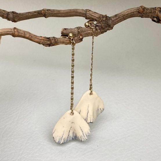 Paire de boucles d’oreilles pendantes en céramique blanche suspendues à une branche.