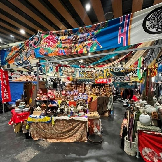 Stand décoré de bannières japonaises colorées avec objets artisanaux et figurines exposés.