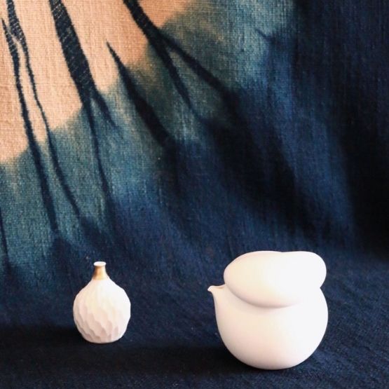 Petites sculptures en bois représentant des chats japonaises, avec des sourires et des colliers, exposées sur un comptoir en bois.