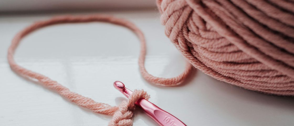 Pelote de laine rose avec un crochet assorti, début d’un ouvrage en mailles chaînettes.